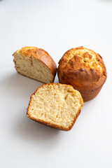 Two muffins on a white surface, one cut in half. The muffins are golden brown and have a slightly crispy texture. Homemade baking and pastry made from wheat flour. Making bread and Easter cakes