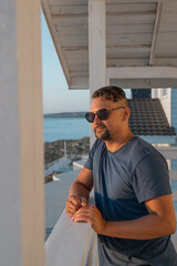 A man in sunglasses swims in a blue pool. Vacation at the hotel by the sea, sunset and mountains. Happy dad, family happiness. Muscles and a beautiful figure, black hair. High quality photo