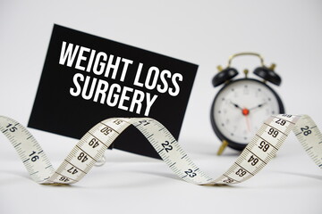 Weight Loss Surgery text with alarm clock and measuring tape on white background
