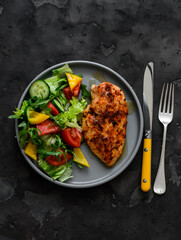 Balanced diet lunch - baked chicken breast and fresh vegetable salad on a dark background, top view