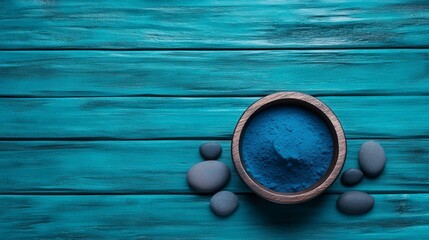 A rustic wooden bowl filled with vibrant blue powder placed on a turquoise wooden surface with smooth stones