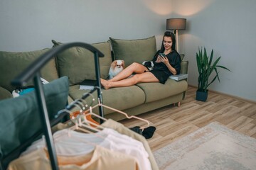 woman relaxing with smartphone during morning beauty routine with japanese chin dogs at home, clothes rack