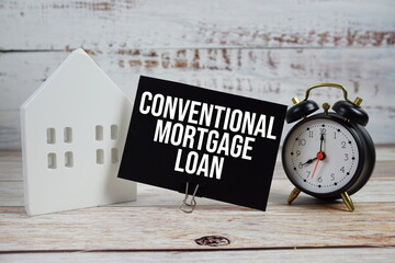 Conventional Mortgage Loan on paper card with alarm clock and white house model on wooden background