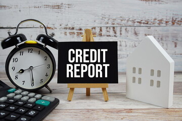 Credit Report on paper card with white house model, and alarm clock on wooden background