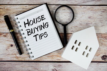 Fototapeta na wymiar House Buying Tips text on paper notebook with white house model and magnifying glass on wood background