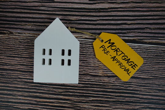 Mortgage Pre-Approval text on price tag with white house model flat lay on wooden background