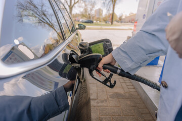 A person fuels a black diesel vehicle at a station, holding the nozzle firmly in the car’s tank opening on a sunny day..