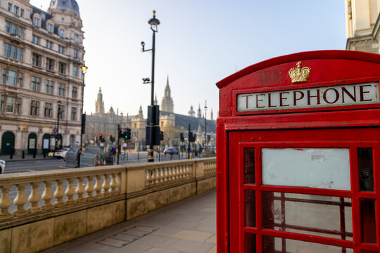 A striking, vibrant red telephone box stands out prominently on a busy London street, with several iconic landmarks visible in the background, showcasing the unique charm and beauty of the city