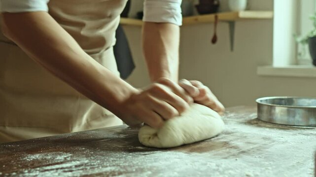 A baker in an apron kneads the dough with his hands and sprinkles it with flour to bake delicious homemade bread.