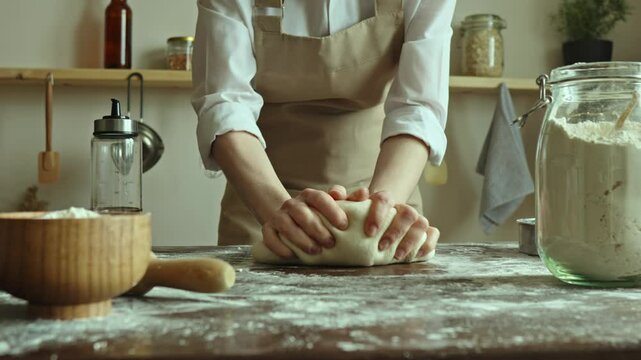 A baker in an apron kneads the dough with his hands and sprinkles it with flour to bake delicious homemade bread.