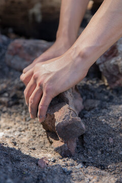 Man preparing camp fire by clearing away ash and charcoal with rock