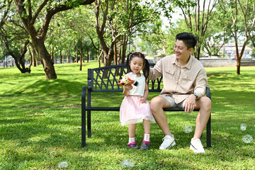 A man and a little girl are sitting on a park bench, Scene is warm and friendly, as the man and the girl seem to be enjoying each other's company. © Stella 16