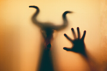 Horror, halloween background - Shadowy figure with horns behind the glass