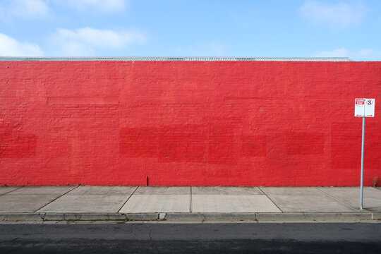 A long red wall with a street sign in front of it