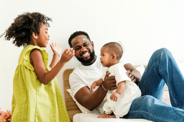 Happy Black father playing joyfully with his two daughters at home, showing authentic family love and bonding. Perfect for Father’s Day, parenting, lifestyle, and diversity-related content.