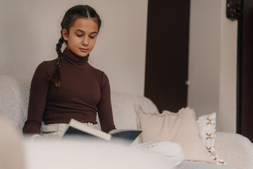 Young girl reading a book on the sofa at home