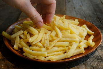 Female hand takes golden french fries from plate. Eating fast food.