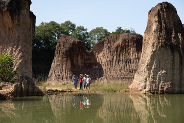 Four Asian senior women walking along pond edge beneath large rock formations in daylight, enjoying...