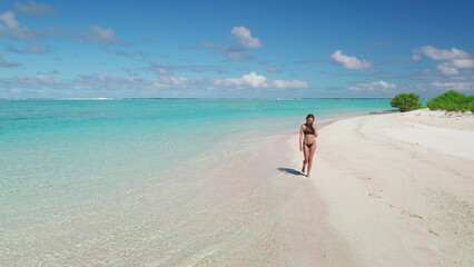 Young woman enjoying her vacation walking on a beautiful pink sand beach in aitutaki, cook islands, a popular tourist destination known for its stunning turquoise lagoon