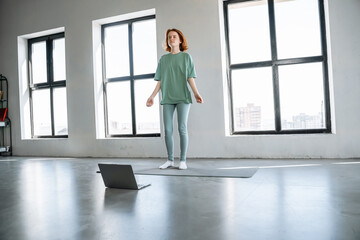 Fototapeta premium A teenager is performing a mountain climber exercise on a mat at home, following an online workout on her laptop. 