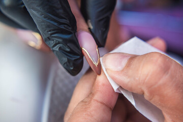 Close-up of a beauty technician using a small towel or lint-free wipe to refine and clean gold...