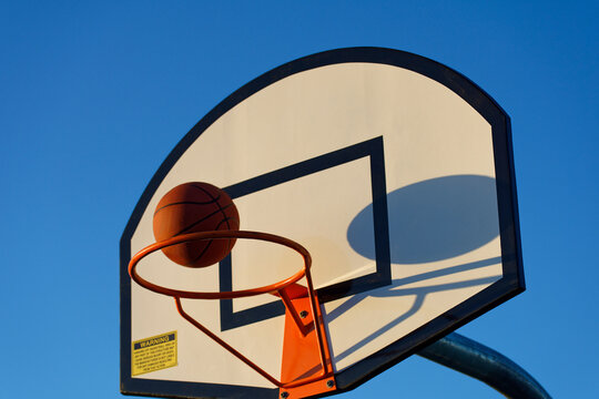 Basketball hoop and ball against a blue sky at sunset at a park