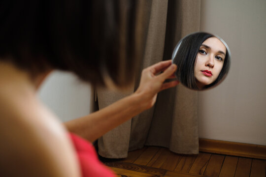 Woman admires reflection in small mirror indoors