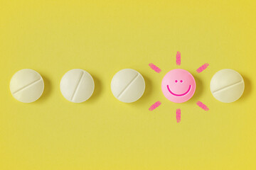Pills in a row and pill with a happy face on yellow background - Concept of medicine, drug therapy and placebo effect