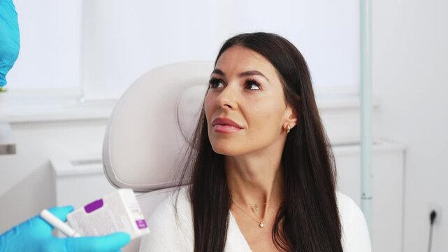 Beautiful brunette woman at beauty medical clinic. She is sitting and talking with female doctor about face aesthetic treatment. She is trustful and happy.