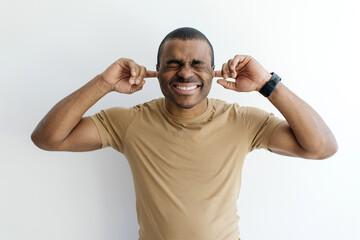 Young dissatisfied annoyed young black man with closed eyes covering ears with fingers, do not want...