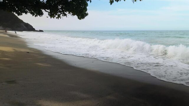 Waves swirl softly at Playa Osma beach, caressing the sandy shore beneath a serene blue sky. The tranquil atmosphere invites relaxation and peace, showcasing nature's beauty.