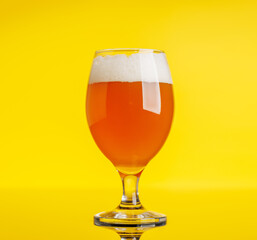 A frothy glass of fresh beer against a bright yellow background