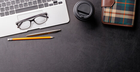 Top view of a dark leather office desk with laptop, supplies, and coffee cup