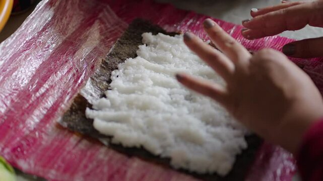 Chef hands gently spread warm shari sushi rice over a nori seaweed sheet on a bamboo makisu mat, using precise sushi‑zaiku technique to prepare makizushi rolls with layer before filling and rolling
