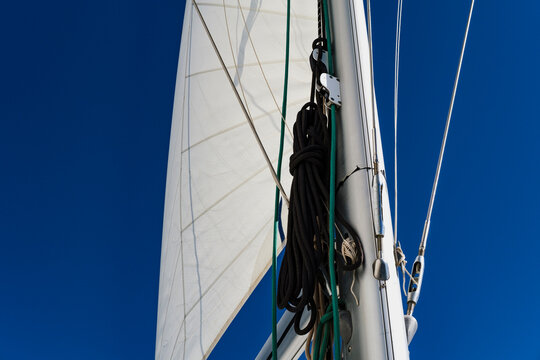 open sails on mast, view from bottom of sail boat, rigging, mast,  deep blue sky