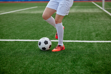 Female legs with soccer ball on green field, red cleats in training action.