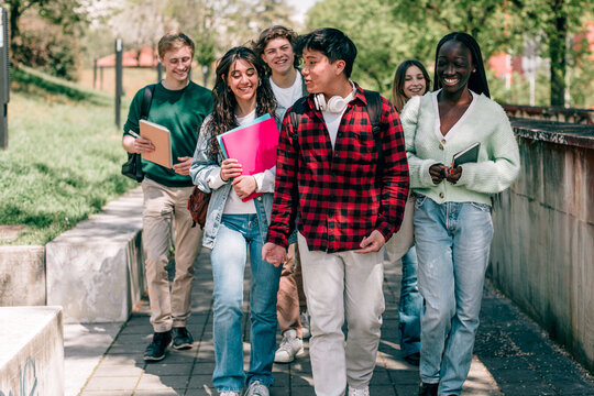 Happy diverse students walking and talking on university campus