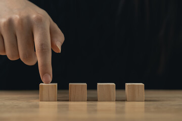 Close-up of Hand Pointing at Wood Blocks on Table with Dark Background, Concept of Choice, Decision...