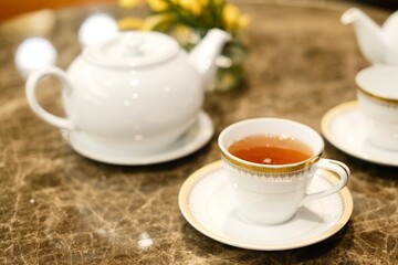 Close-up of a fine bone china teacup with gold trim and a pot of Taiwanese tie guan yin oolong tea...