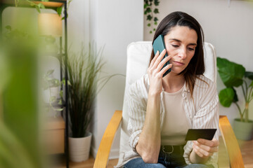 Worried woman on phone call holding credit card at home