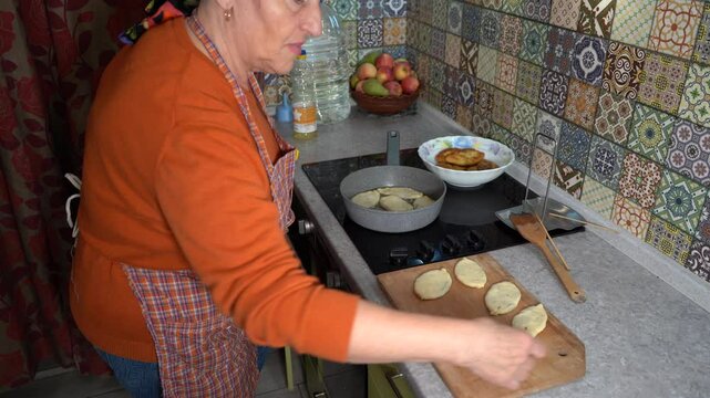 A woman is frying pies. Cooking fried food at home. Grandma cook at Kitchen stove