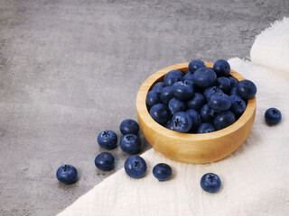 Blueberries in wooden bowl with cloth on stone texture background