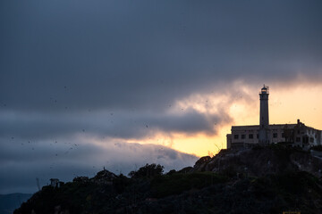 Tower of Alcatraz standing alone against a cloud-draped horizon glowing with golden sunset light...