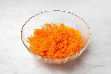 Grated fresh carrots in glass bowl on light textured background, healthy vegan food ingredient, for healthy food recipes, salads, and vegan meal preparation