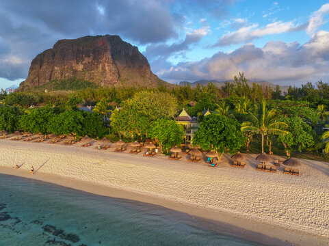 Thatched umbrellas and sunbeds line a quiet beach in front of tropical villas in Le Morne, Mauritius