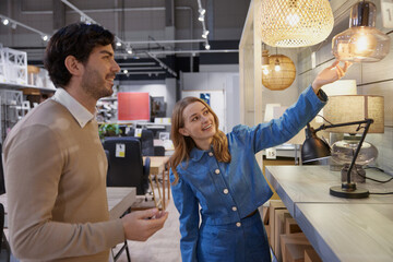 Young couple actively exploring various trendy lighting options in contemporary furniture store