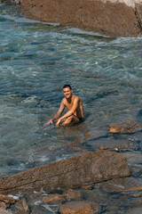 Chico joven tatuado en la playa de rocas, Playa de la Arnía, Santander, España