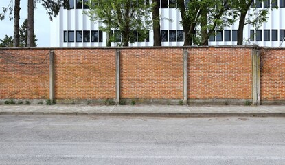 Surrounding brick wall with trees and white modern building on behind. Concrete sidewalk and  street in front. Background for copy space © luca piccini basile
