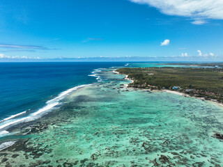 Top-down view of white sand beach, umbrellas and shallow reef-filled turquoise waters in Le Morne