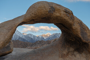 Mobius Arch curves dramatically toward the left as it frames the snowy Sierra Nevada beneath a calm...